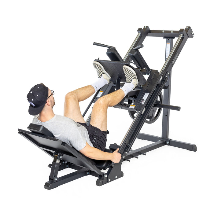 Wearing athletic gear, a person lies on the padded seat of the Bells of Steel Leg Press Hack Squat Machine, pressing the black angled footplate upward with both feet—an ideal addition to any home gym.