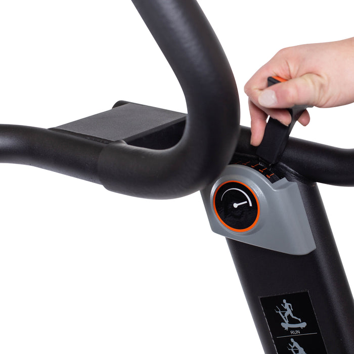 A hand adjusts the resistance knob on the console of the Bells of Steel Blitz Magnetic Resistance Manual Treadmill, featuring handlebars and a digital display.