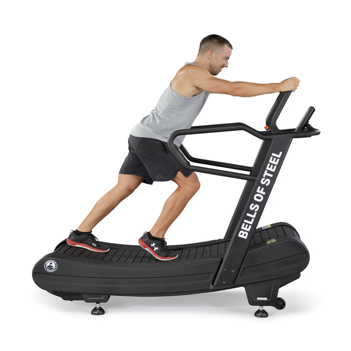 A man in athletic wear runs on the Blitz Magnetic Resistance Manual Treadmill by Bells of Steel, gripping the front handles as he exercises on this curved manual treadmill.