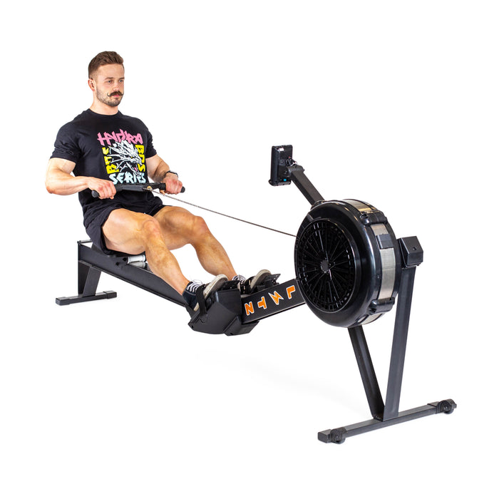 A person in a black T-shirt is demonstrating the rowing motion on a Blitz Air Rower by Bells of Steel, positioned on a white background. The machine exemplifies low-impact cardio and offers a full-body workout.