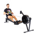 A person in a black T-shirt is demonstrating the rowing motion on a Blitz Air Rower by Bells of Steel, positioned on a white background. The machine exemplifies low-impact cardio and offers a full-body workout.