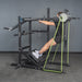 A person prepares to squat in a gym using the Bells of Steel USA Pandemonium Squat – a 3-in-1 pendulum squat, calf press, and Viking press machine – standing on its slanted platform and gripping the handles.