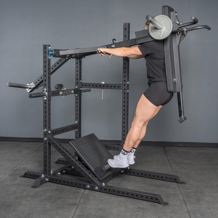 A person uses the Bells of Steel USA Pandemonium Squat – 3-in-1 Pendulum Squat / Calf Press / Viking Press Machine, leaning on padded supports and holding side handles while standing on the slanted footplate against a gray wall.