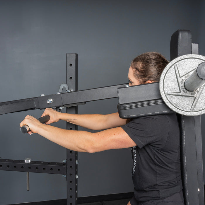 A person uses the Bells of Steel USA Pandemonium Squat—3-in-1 Pendulum Squat, Calf Press, and Viking Press Machine with metal weight plates and padded backrest. The home gym scene has a plain gray wall background.